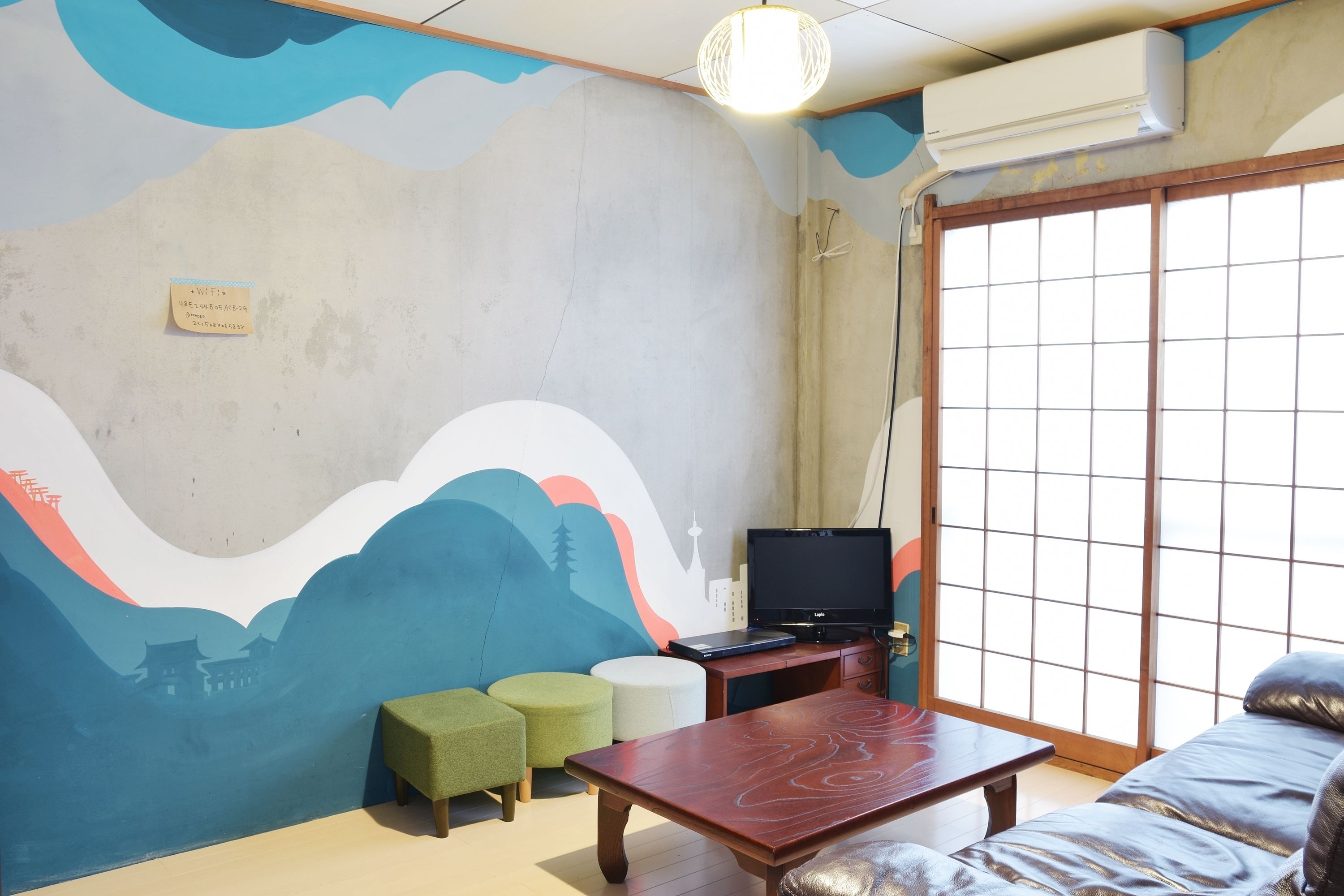 A room with a traditional Japanese-style sliding door, a flat-screen TV on a wooden table, and a mural on the wall depicting a mountain landscape.