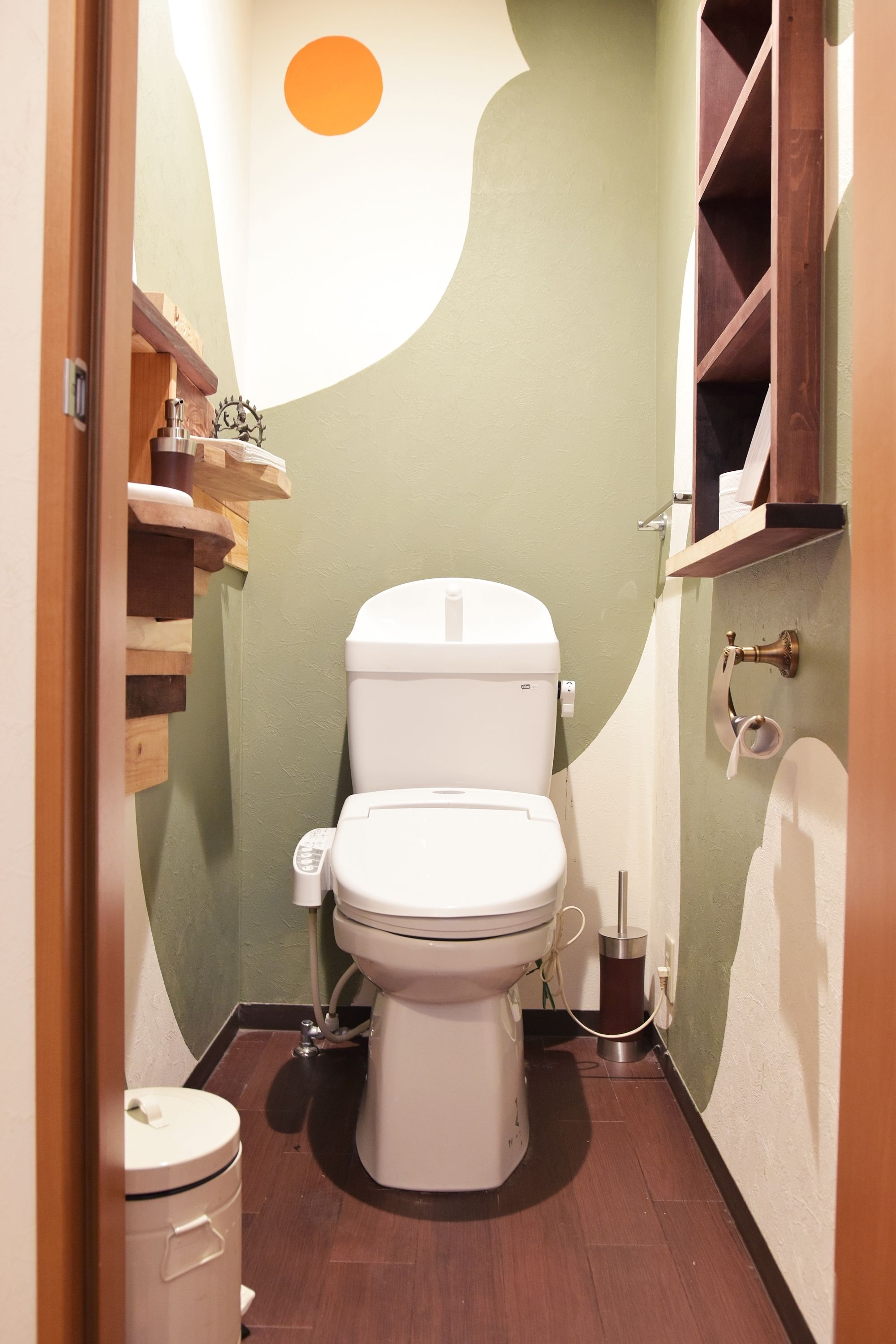 A small bathroom with a toilet, a sink, and a wooden shelf with toiletries.