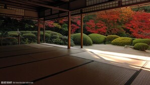 Una habitación japonesa tradicional con suelo de tatami, vigas de madera y vistas a un jardín con follaje rojo.