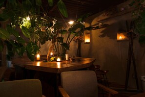 A dimly lit dining area with a wooden table, chairs, and hanging plants. - Lund house - Hostel (Kyoto)