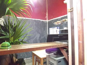 A small, enclosed workspace with a wooden desk, a computer, and a chair. A large potted plant is visible to the left. - Lund house - Hostel (Kyoto)