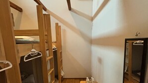 Un pasillo estrecho con suelo de madera, un banco de madera, una lámpara colgante, un espejo montado en la pared y un equipo de aire acondicionado.