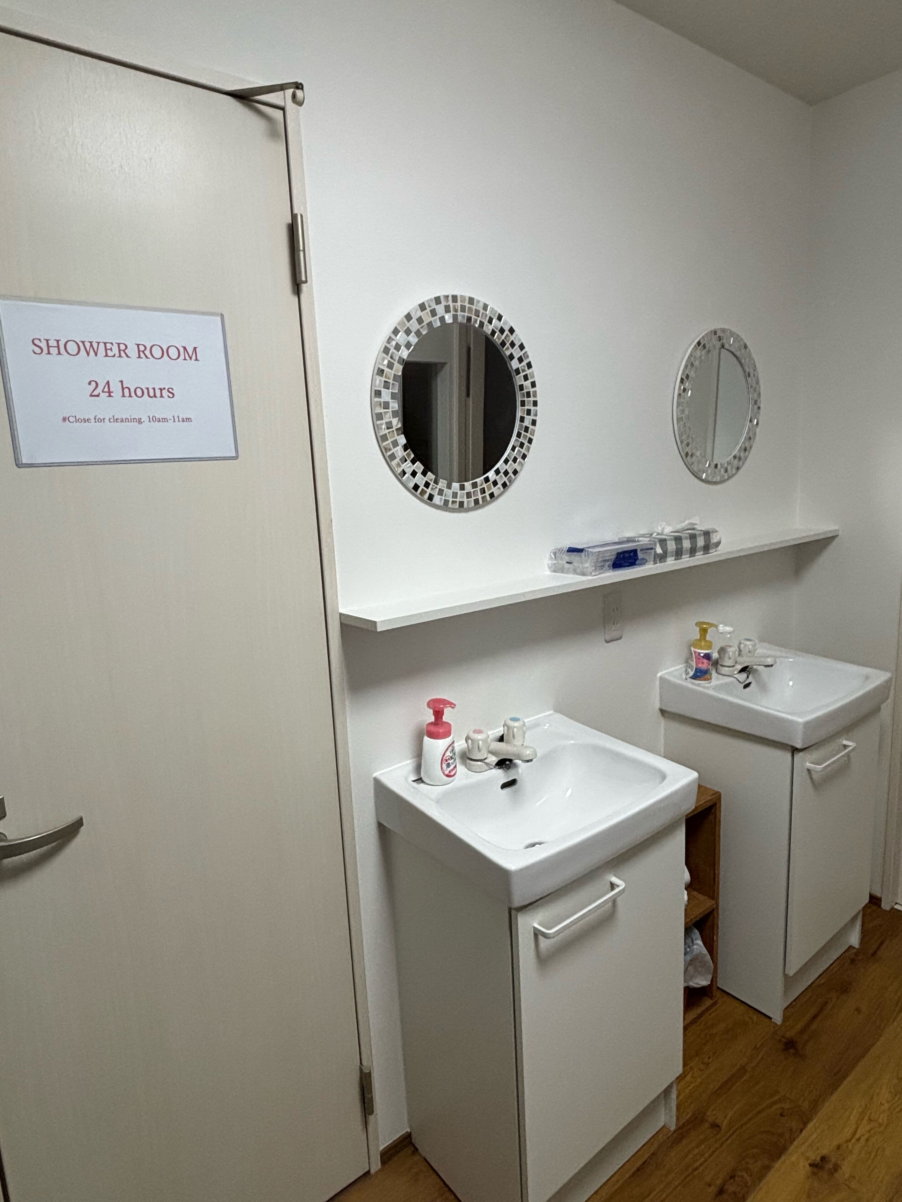 A bathroom with a shower room sign, two sinks, a mirror, and a shelf with toiletries.