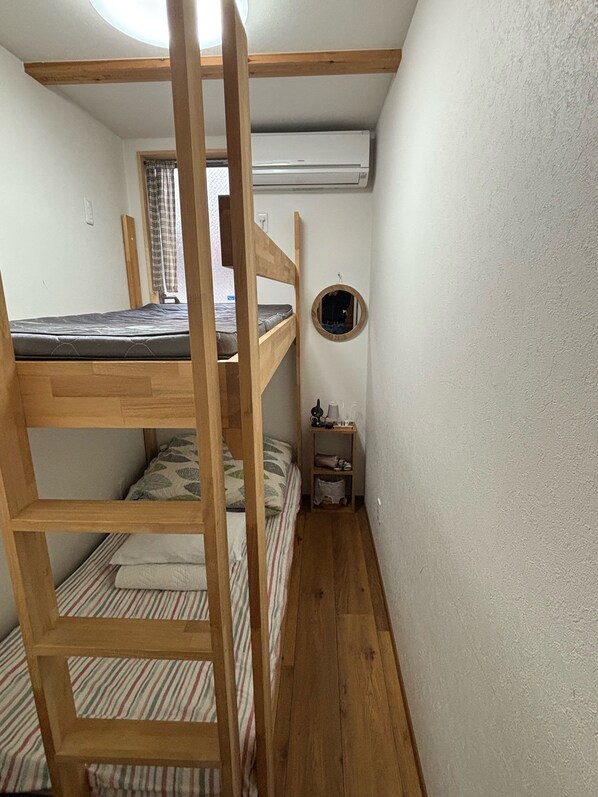 A compact room with a bunk bed, a small bedside table, a mirror, and an air conditioning unit.