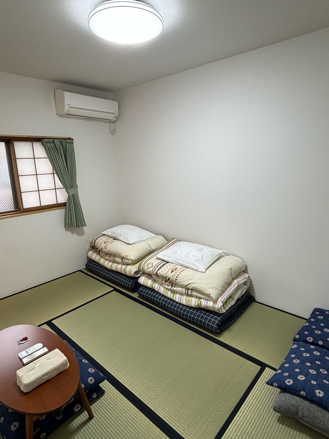 Une pièce comprenant un lit, un futon, des tatamis, une table avec une télécommande et un climatiseur.
