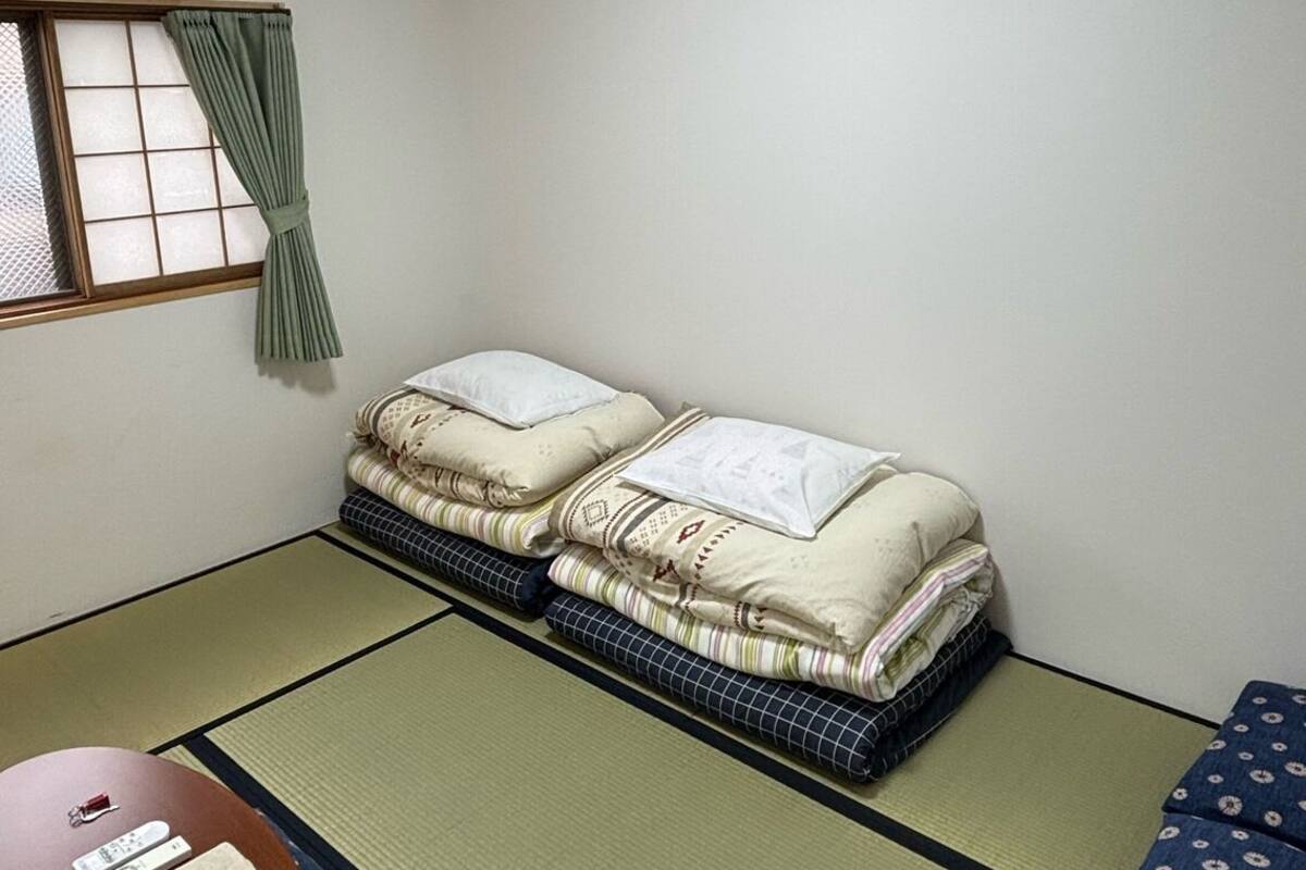 Une pièce comprenant un lit, un futon, des tatamis, une table avec une télécommande et un climatiseur.