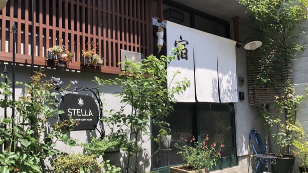 Un edificio con un letrero que dice "STELLA NAZAWA GUEST HOUSE" y un amplio toldo blanco con caracteres chinos.