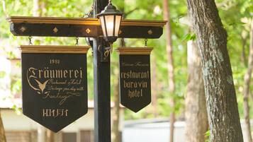 Två hängande skyltar för en restaurang och ett hotell, båda med en retrodesign och guldfärgad text.
