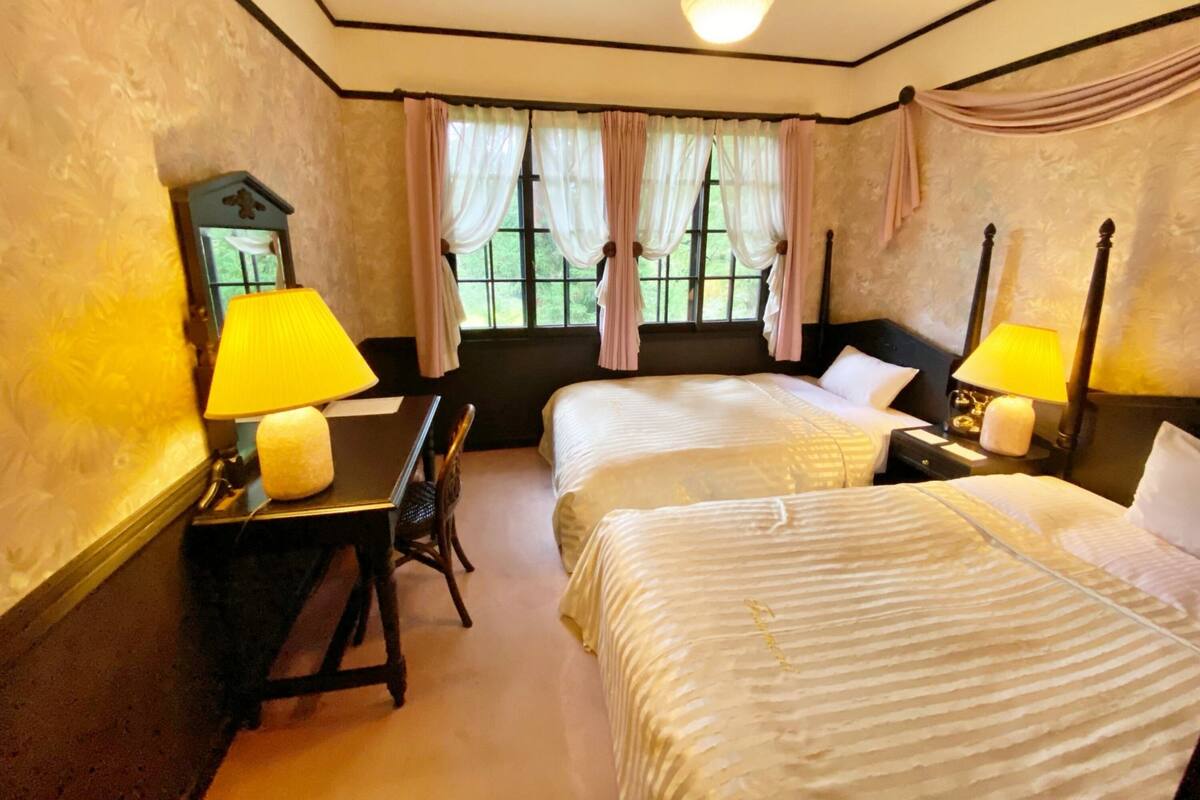 A hotel room with two beds, a desk, a chair, and a nightstand with lamps.