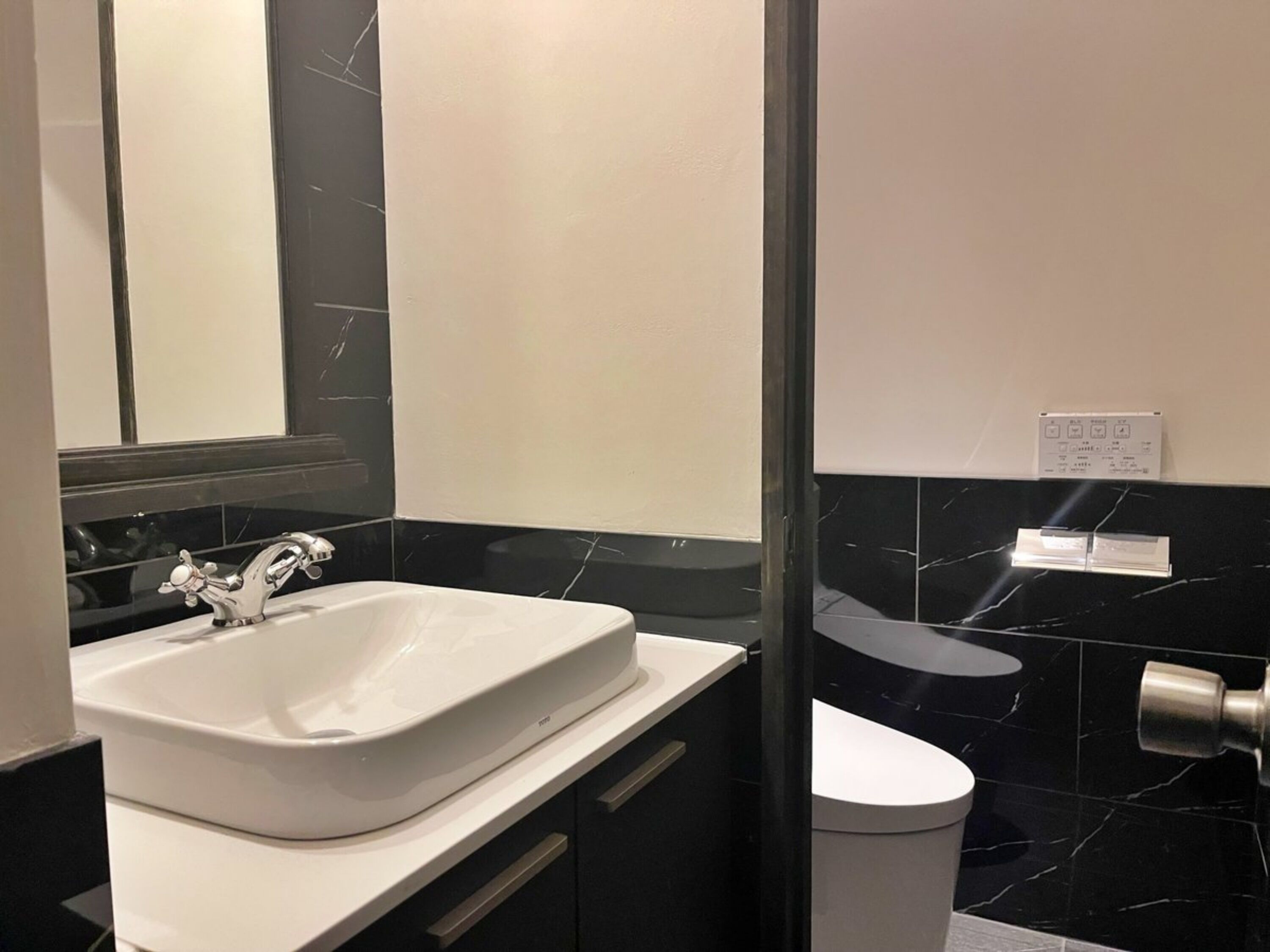 A modern bathroom with a white sink, black marble backsplash, and a toilet.