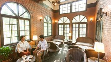 A cozy indoor seating area with wicker furniture, large windows, and a brick wall.