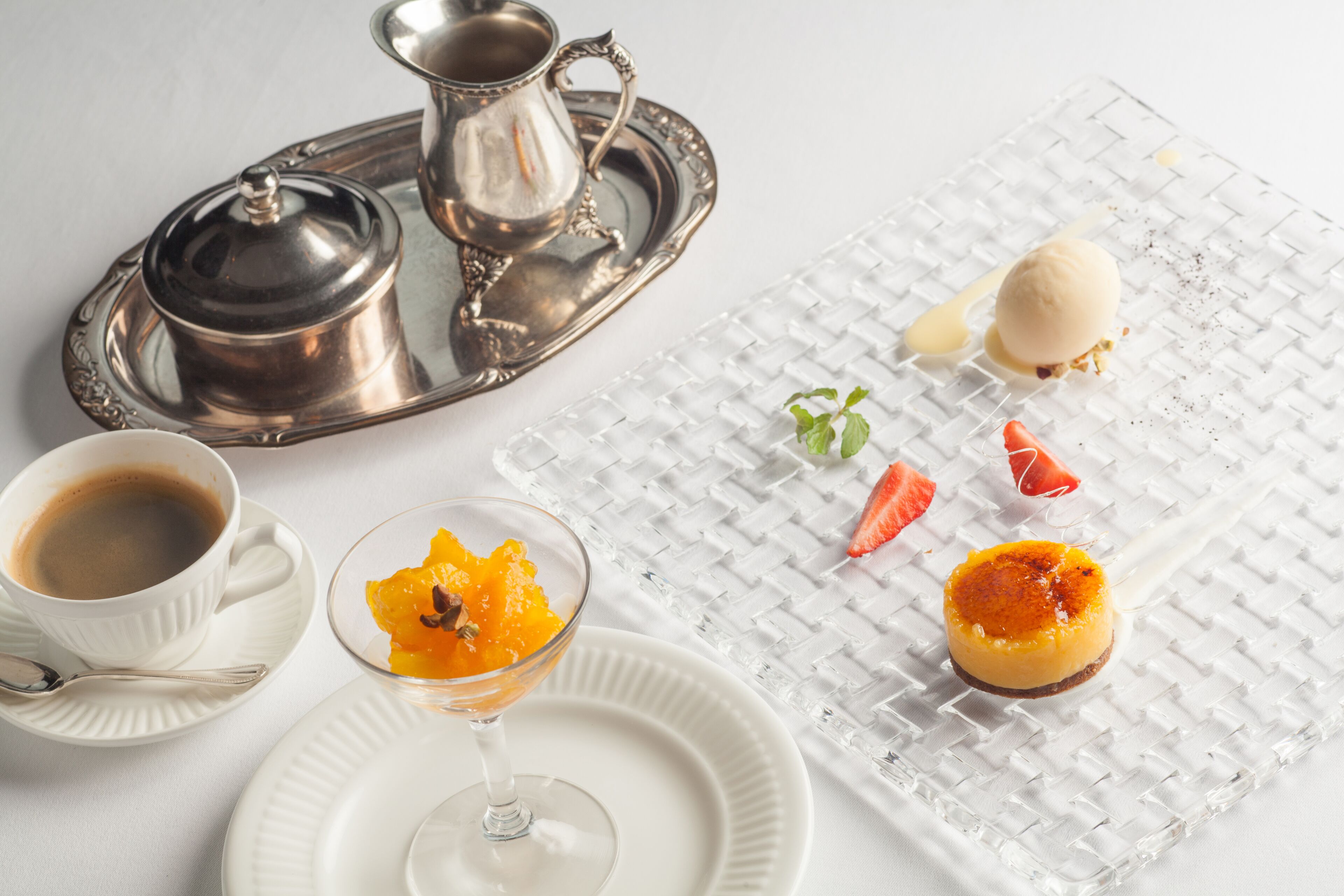 Een dienblad met een zilveren karaf en beker, een glas sinaasappelsap, en een dessertbord met ijs en fruit.