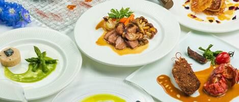 A variety of dishes on white plates, a wine bottle, and a glass of wine.