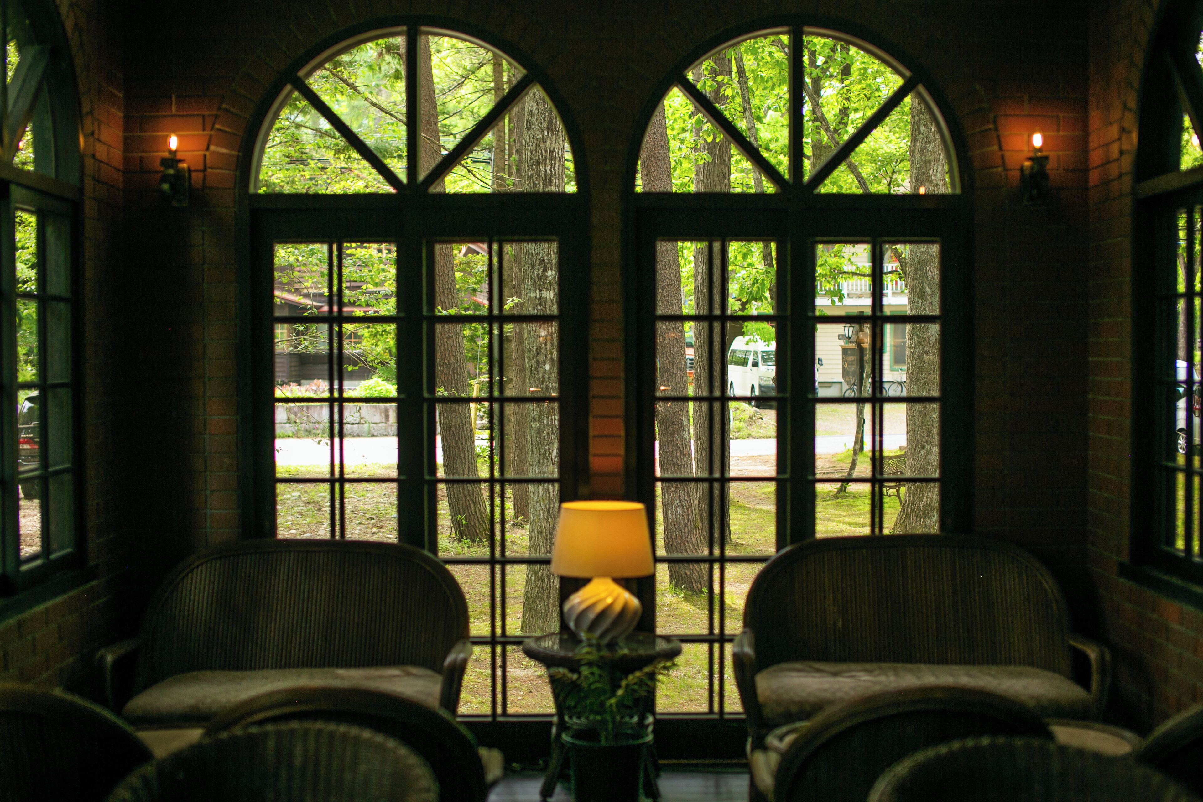 A room with two arched windows, a lamp on a table, and two wicker chairs.