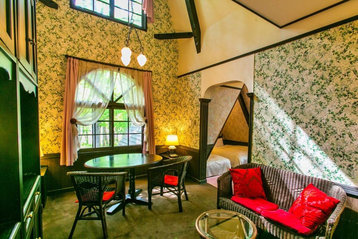 A room with a four-poster bed, a round table with chairs, a wicker sofa with red cushions, and a small glass table.