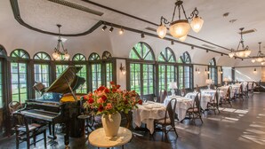 A spacious room with a grand piano, tables set for dining, and large arched windows allowing natural light. - Restaurant & Hotel Traumerei (Hakuba)