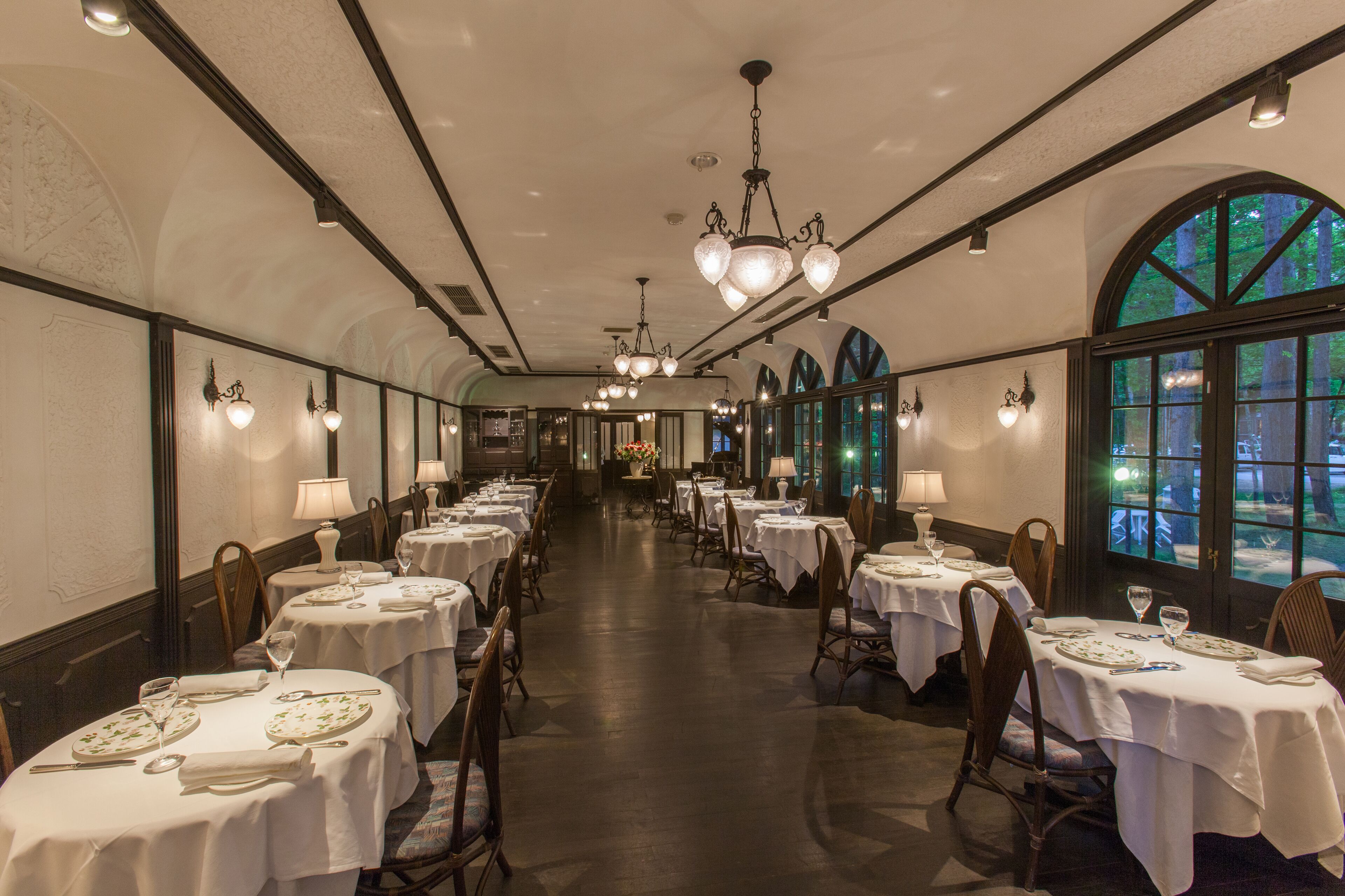 A long dining hall with tables set for service, large windows, and chandeliers.