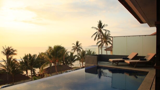 A infinity pool with lounge chairs, palm trees, and a view of the ocean at sunset. - Lima Satu Resort (Pemenang)