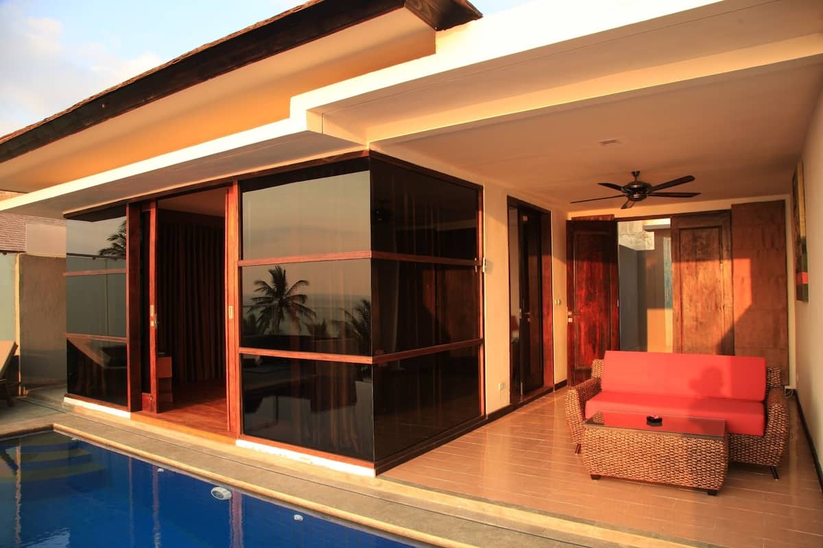A modern house with a swimming pool, large glass doors, and a red sofa.