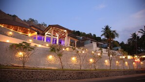 A modern hotel with a stone facade, multiple levels, and outdoor lighting. - Lima Satu Resort (Pemenang)