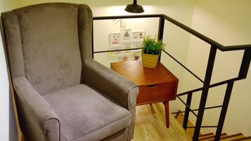 A room with a grey armchair, a wooden side table with a plant, and a staircase with black railings.