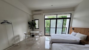 A hotel room with two beds, a small table with chairs, a potted plant, and a large window with a view of greenery. - On My Way Taitung Hostel Backpacker (Taitung)