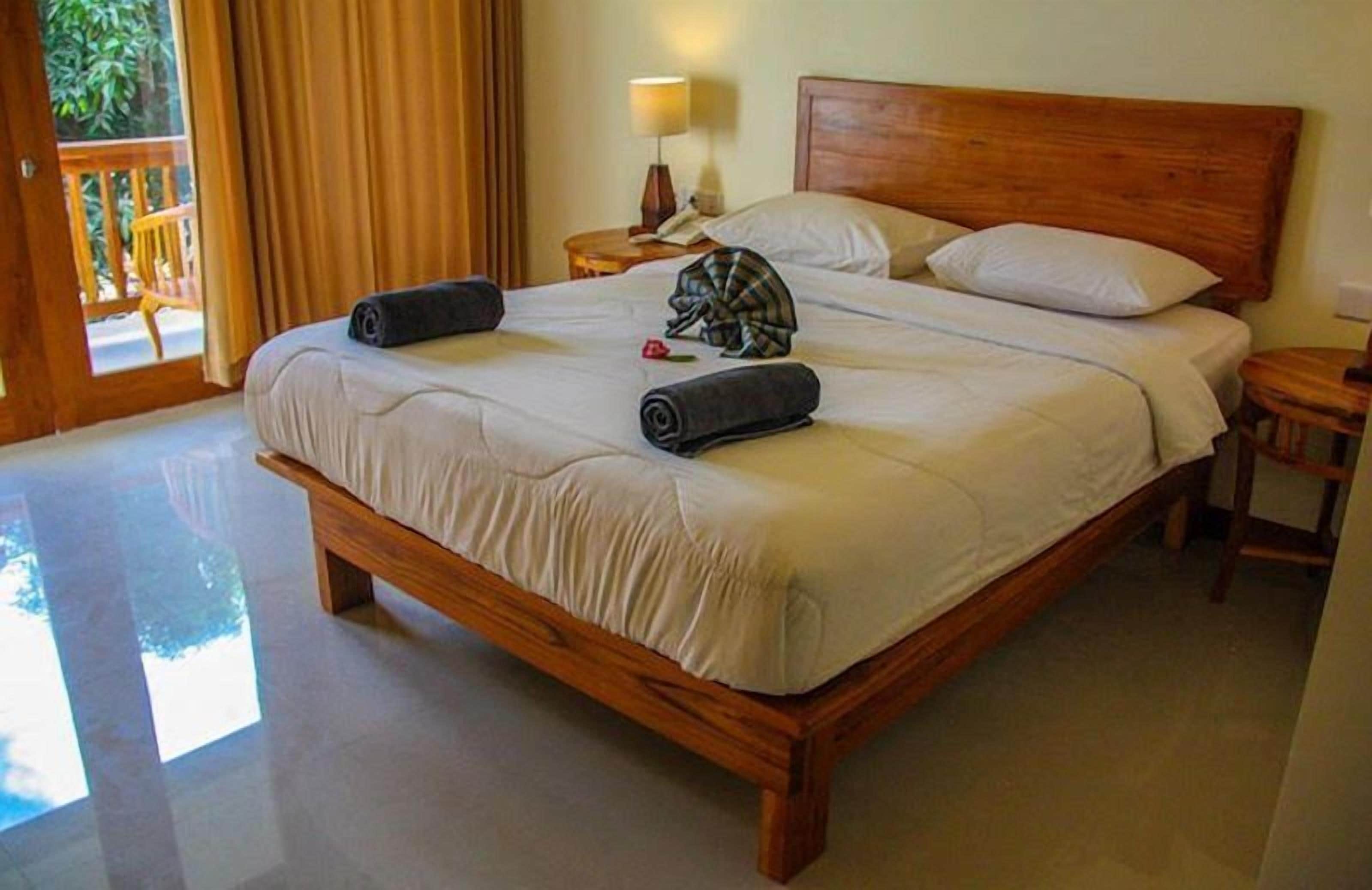 A large wooden bed with white linens, a wooden headboard, and a nightstand with a lamp.