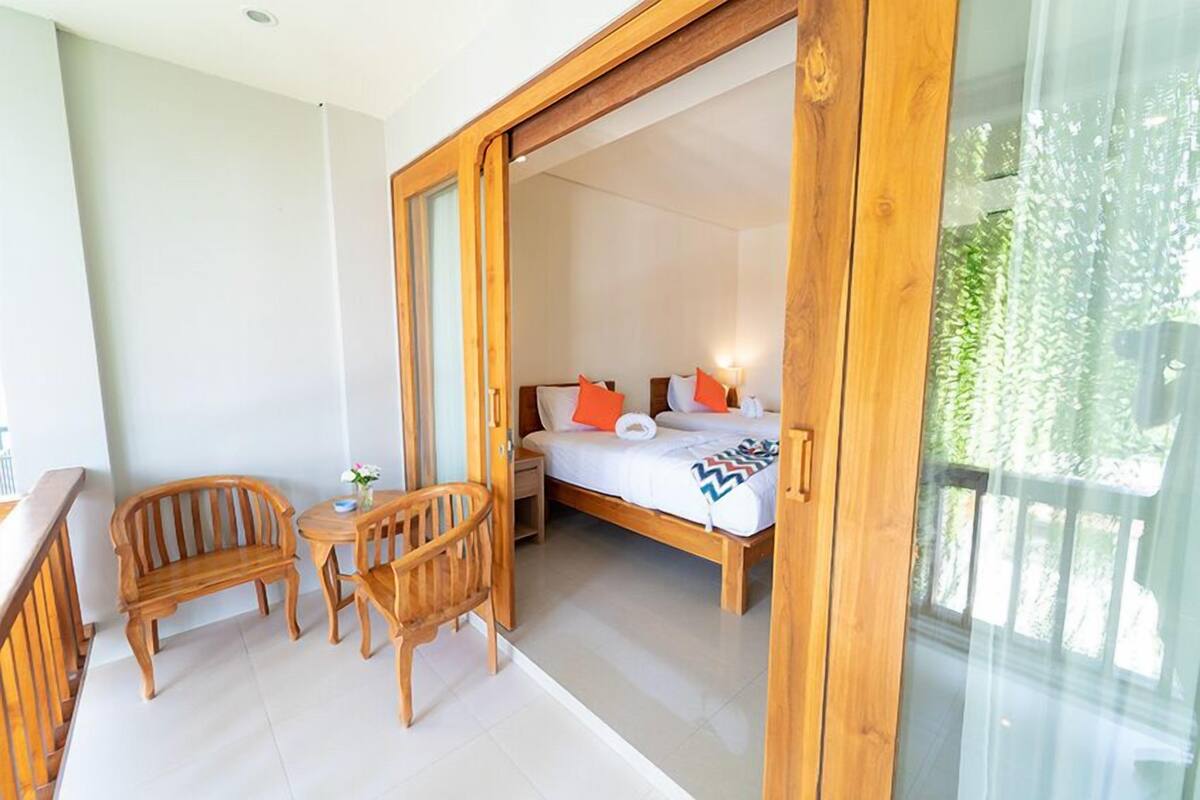A balcony with wooden furniture, a bed with pillows, and a view of greenery.