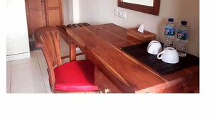 A wooden dining table with benches, a red cushioned chair, a mirror, and two bottles of water. - Komodo Lodge (Labuan Bajo)