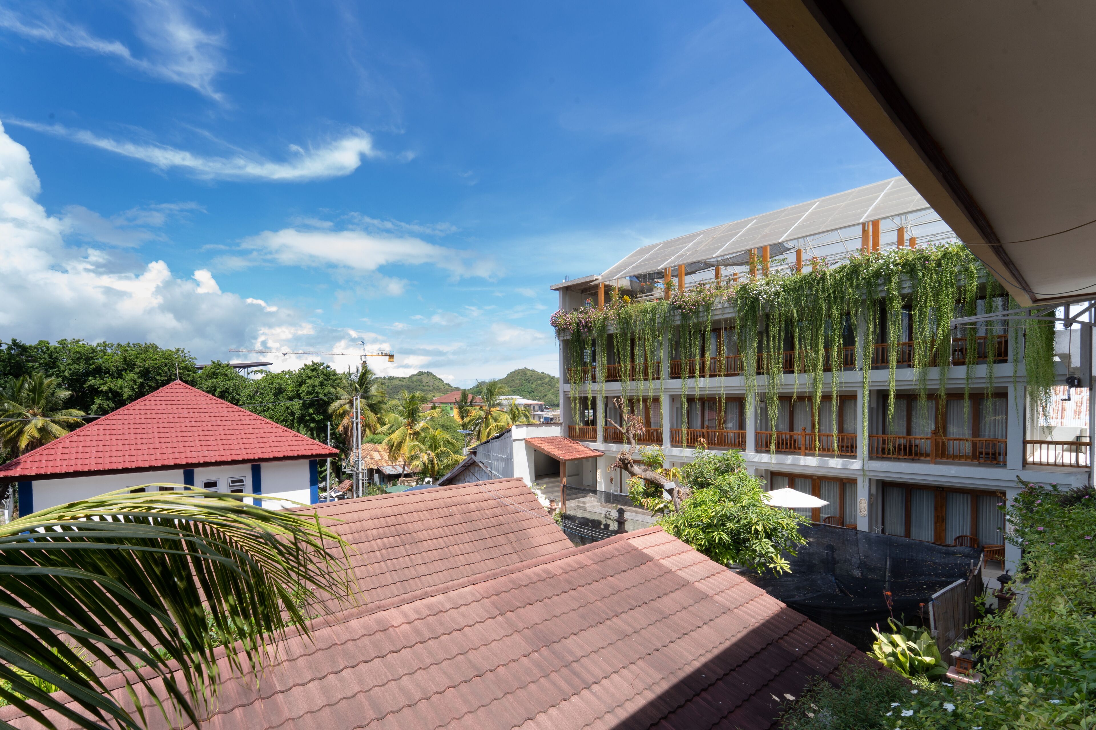 A multi-story building with a red roof and a balcony with hanging plants.