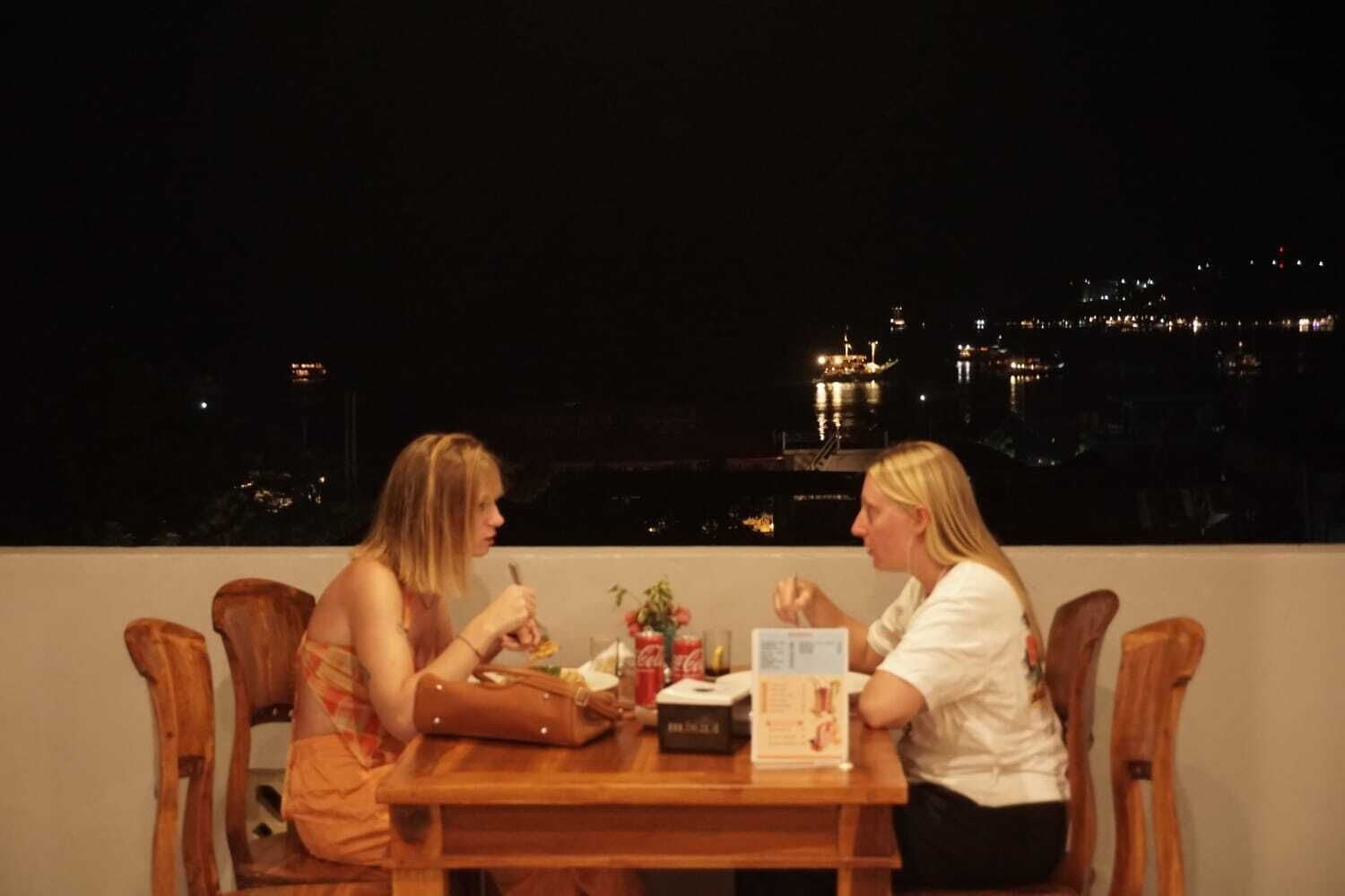 Dos personas cenando en una mesa con vista a la ciudad de noche.