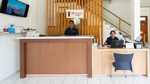 A reception desk at Komodo Lodge with a wooden backdrop, a TV screen, and a sign indicating the location of the toilet. - Komodo Lodge (Labuan Bajo)