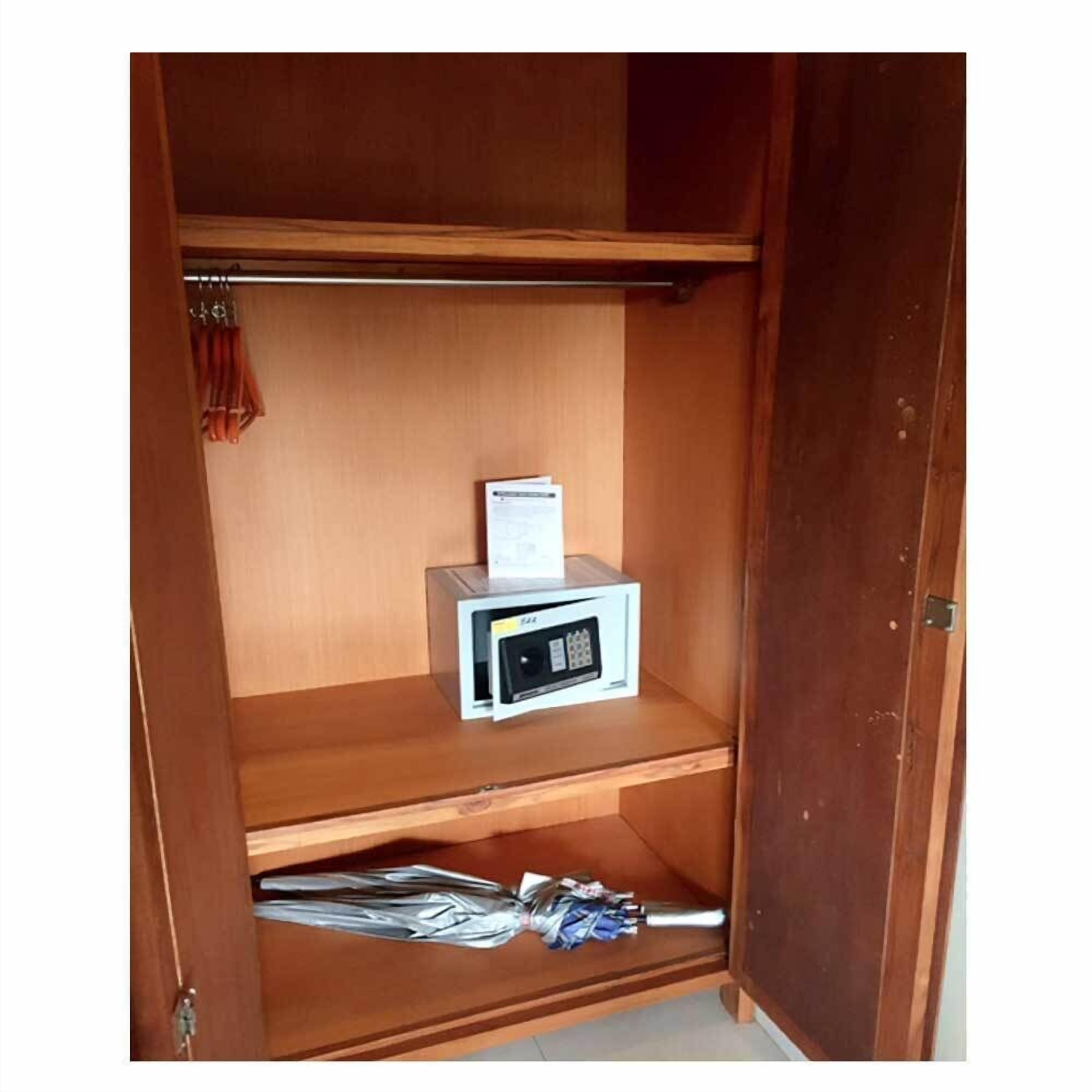 A wooden wardrobe with a microwave on the middle shelf and a pair of shoes on the bottom shelf.