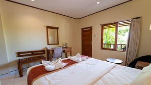 A hotel room with a large bed, a desk with a chair, a small round table, a wooden bench, a window with curtains, and a door. - Komodo Lodge (Labuan Bajo)