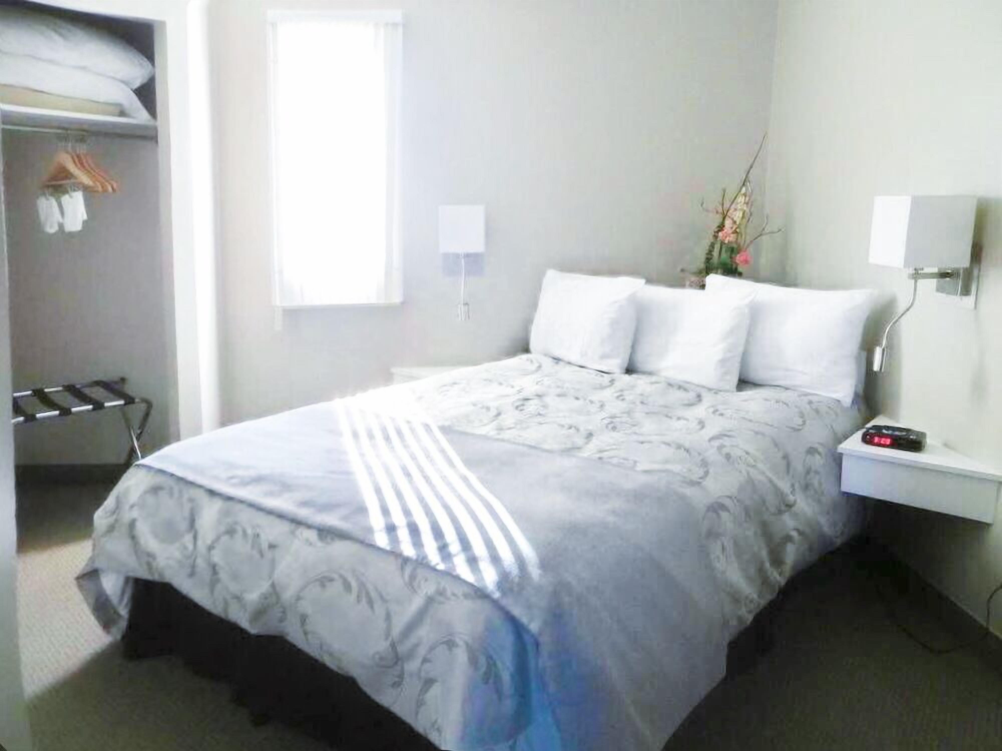 A hotel room with a bed, a nightstand, a lamp, a window, and a wardrobe.