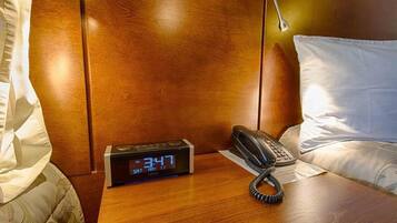 A wooden nightstand with a digital clock displaying 3:47, a telephone, and a pillow.