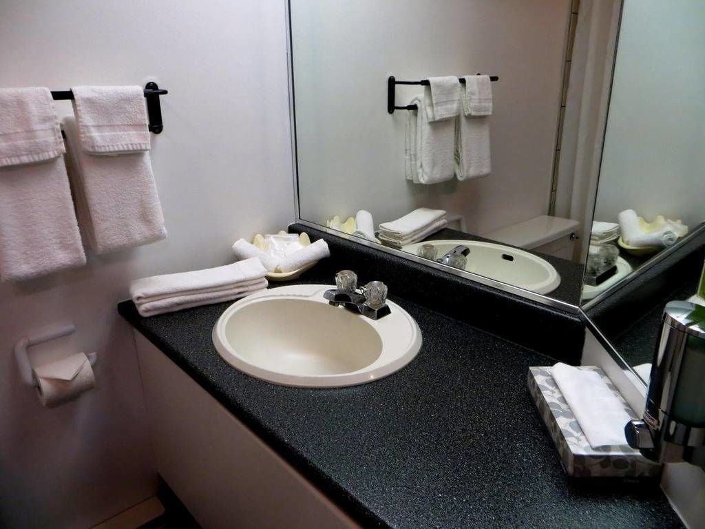 Un baño con lavamanos blanco, encimera negra y un espejo que refleja toallas y artículos de aseo.