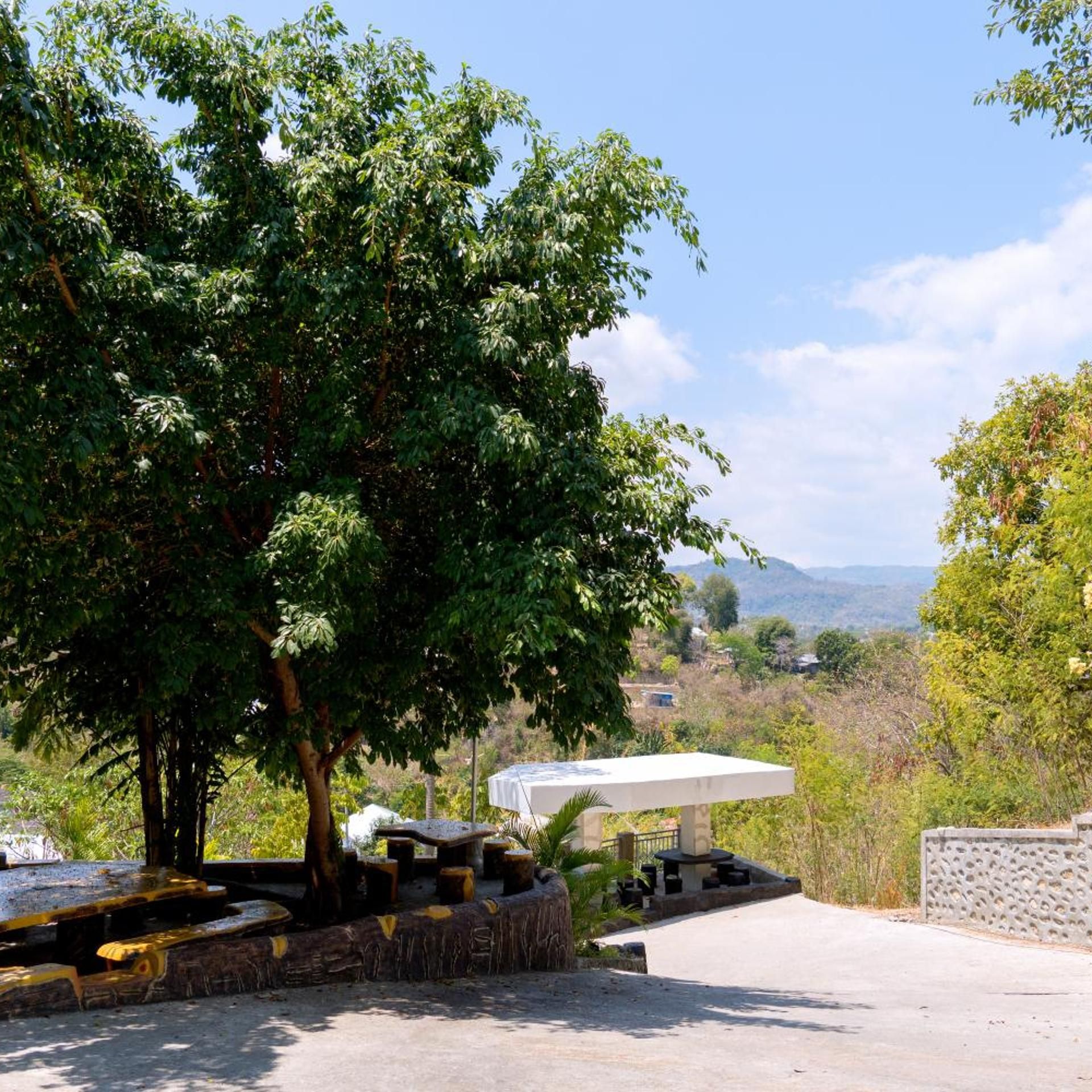A paved area with a table and chairs, surrounded by trees and a view of distant hills.