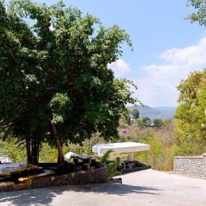 A paved area with a table and chairs, surrounded by trees and a view of distant hills. - Hotel Green Prundi (Labuan Bajo)