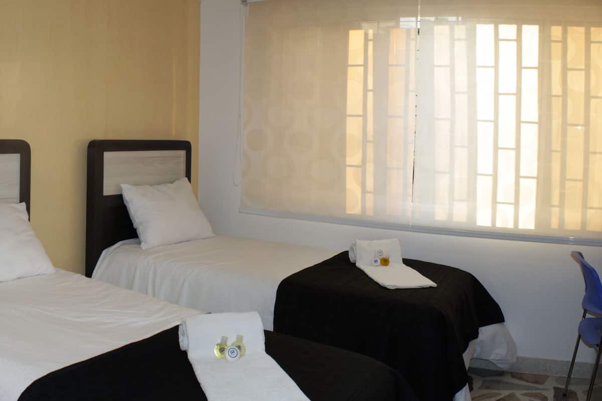 A hotel room with two beds, a nightstand with a phone, a window with blinds, and a chair.