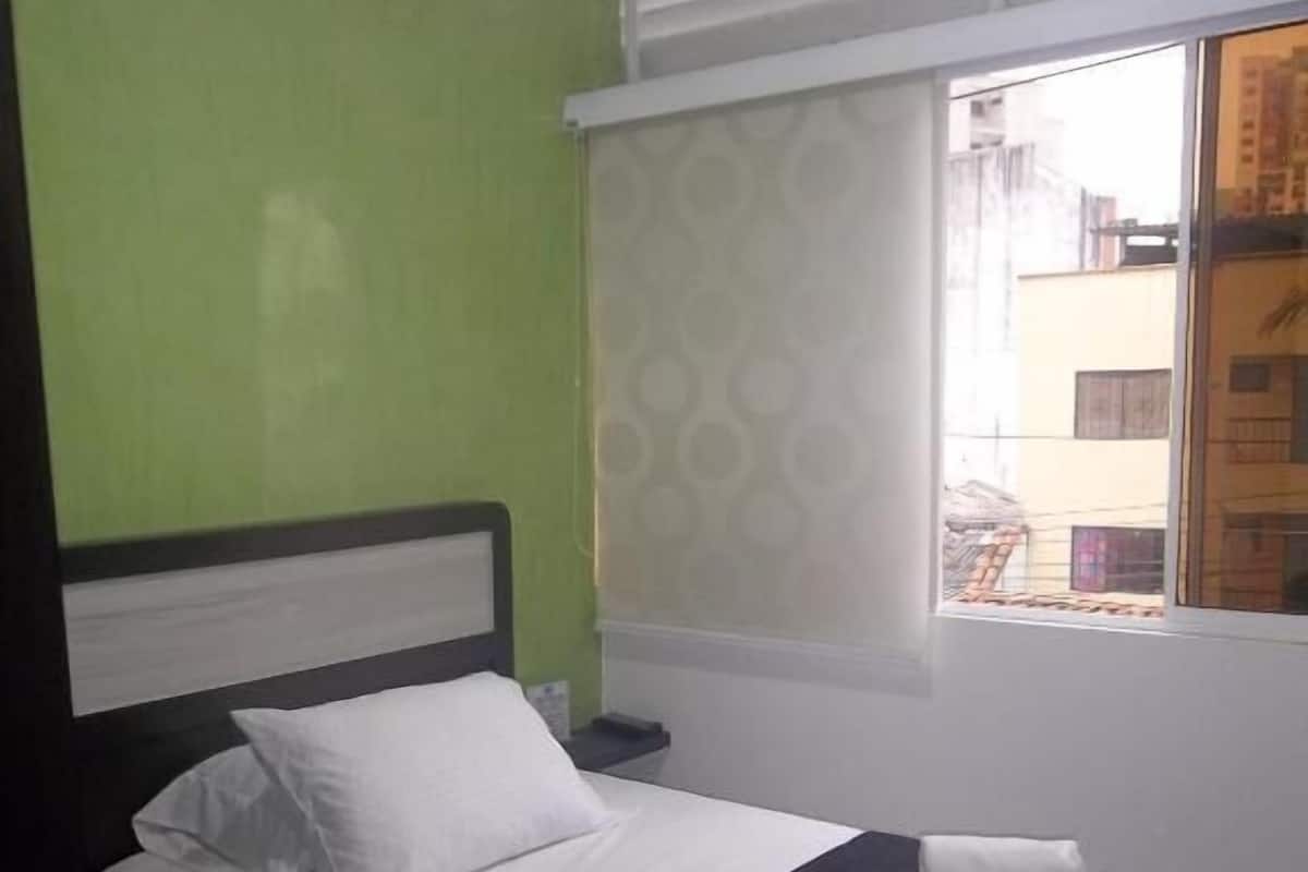 A hotel room with a bed, a desk, and a window with blinds.