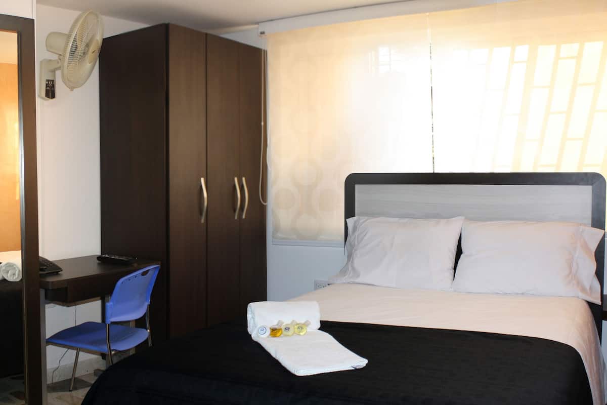 A hotel room with a bed, a desk, a chair, and a wardrobe.