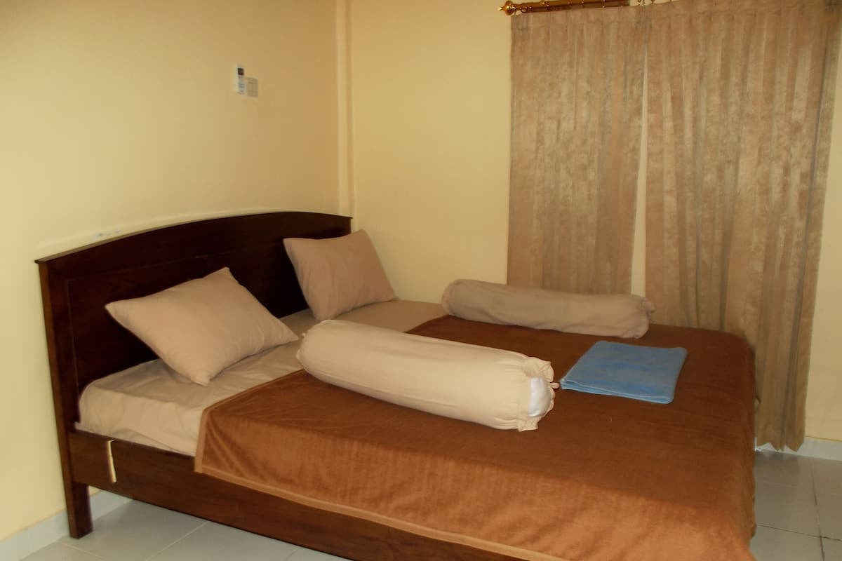 A neatly made bed with a brown headboard and beige bedding in a room with plain walls and a curtain.