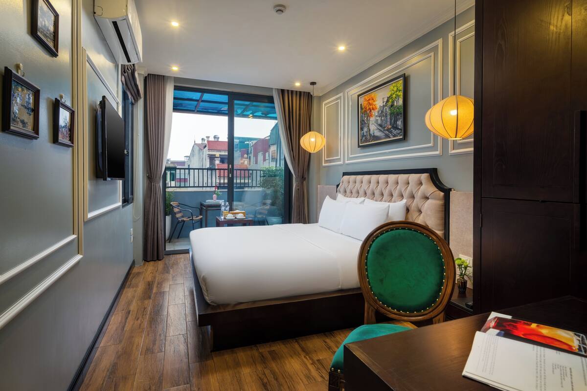 Habitación de hotel con una cama grande, un escritorio con silla, vista a través de un ventanal y un balcón.