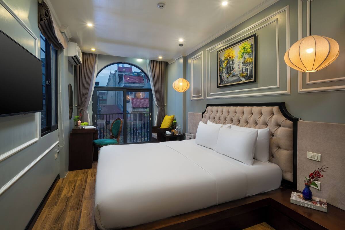 Habitación de hotel con una cama grande, televisión, un cuadro y vistas a la ciudad.