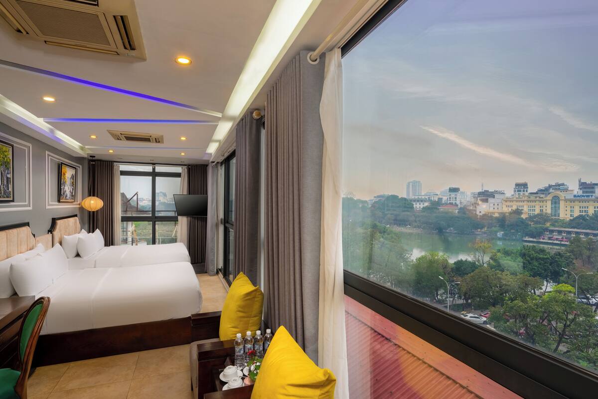 Habitación de hotel con una cama grande, un escritorio con silla, vistas a la ciudad y una ventana con cortinas.
