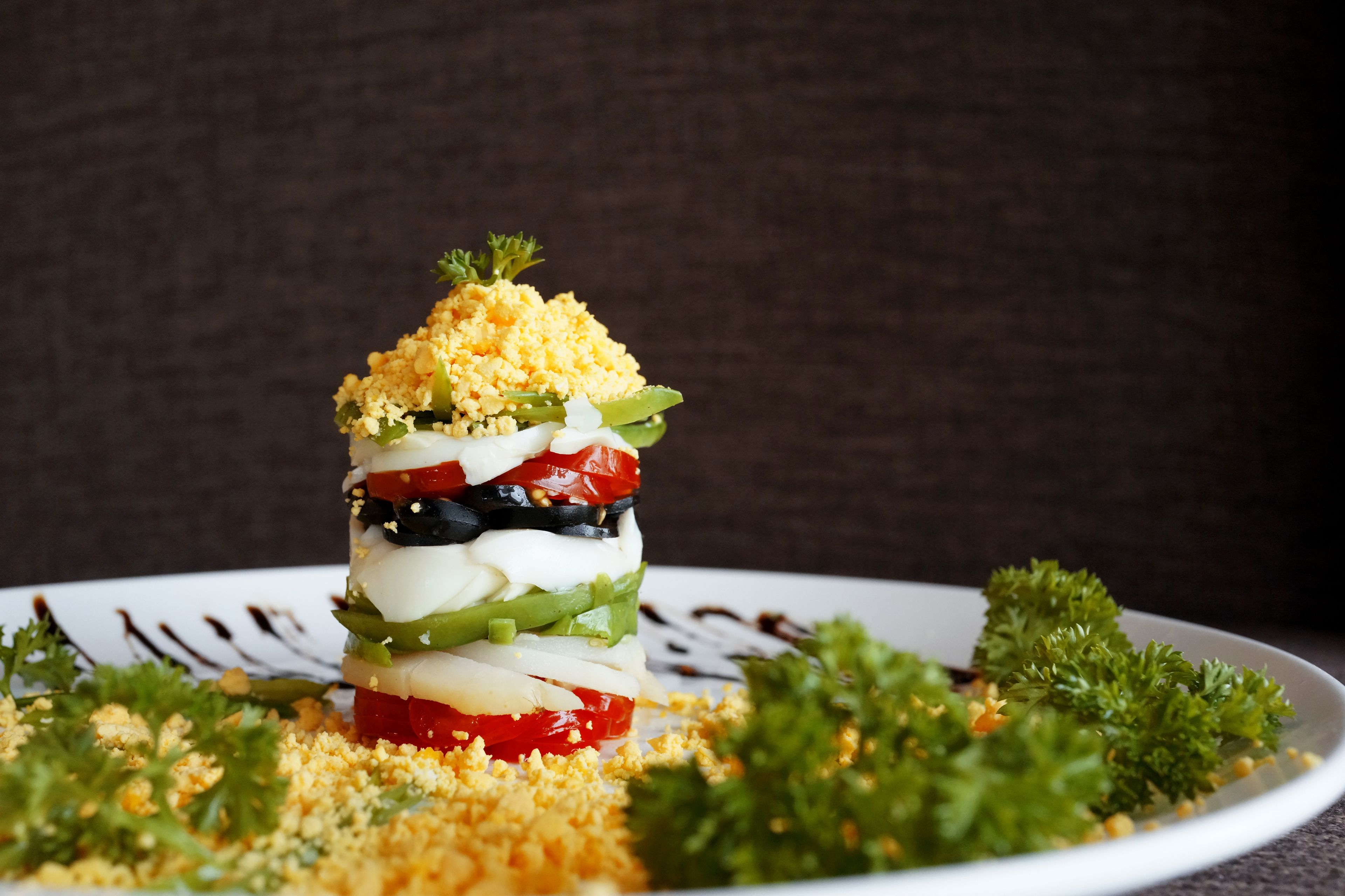 A layered salad with various vegetables and a crumbly topping, served on a white plate with parsley garnish.