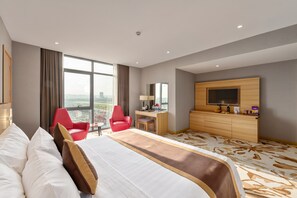 A hotel room with a large bed, a desk, a TV, and a view of the city.