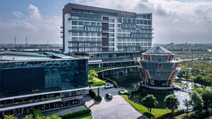 A modern hotel with a prominent glass facade, a central courtyard with a unique architectural structure, and a surrounding landscaped area. - The Reed Hotel (Ninh Binh)