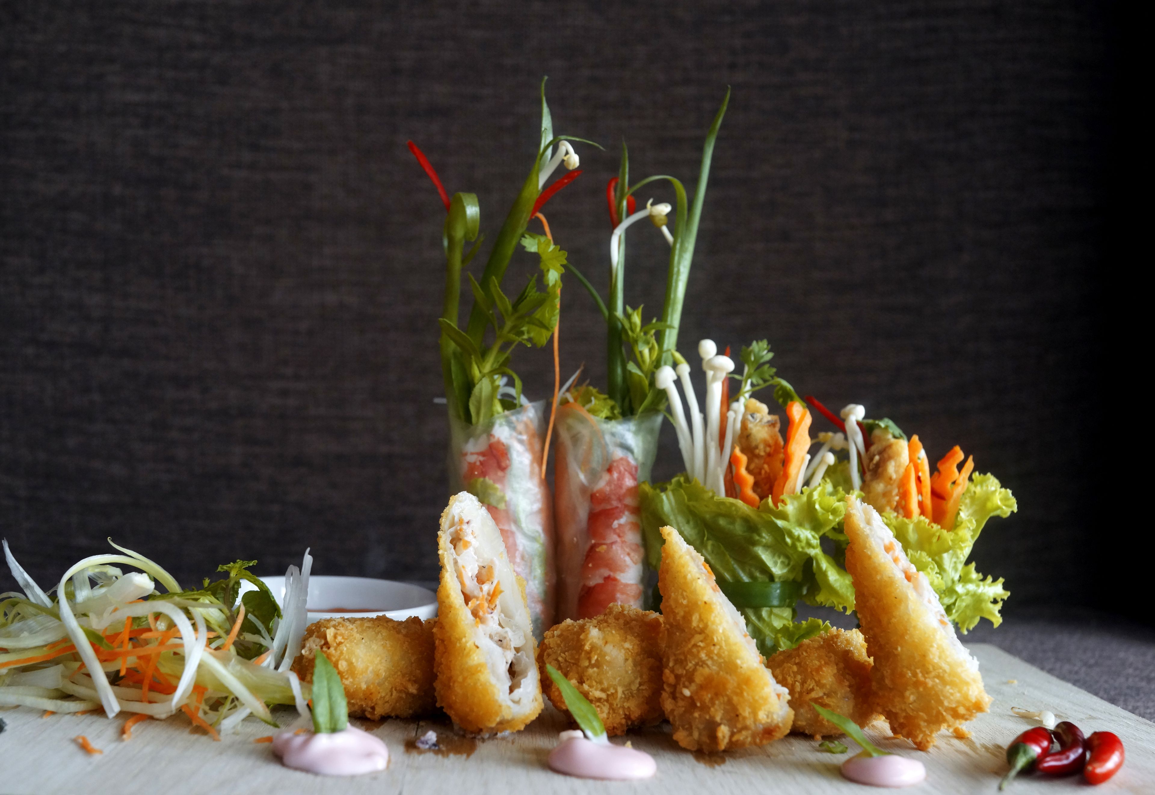 Un assortiment de plats comprenant des rouleaux de printemps, des fritures et une salade composée de légumes et d’herbes aromatiques.